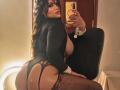 CandyLatina69 with big ass, large tits, wearing black lace thong and fishnet stockings, taking a mirror selfie with her phone, long wavy black hair, black long-sleeve top.