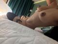 NicoColeman lying on a bed, topless with big tits, black panties, and black thigh-high socks, her nipples and areolas visible, in a dimly lit room.