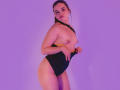 AnabelleRoss with topless, small tits, wearing black high-cut panties, holding yellow strap, purple-lit, standing, brown hair in ponytail, pink lips, looking at camera, sexy, confident pose.
