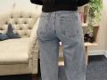 Dalaila's ass in blue, slightly baggy jeans with visible back pockets, standing in front of a beige tufted sofa. Her black top is just above her waist.