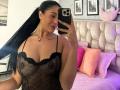 CassieFox with black hair in a ponytail, wearing a sheer black lingerie top, showing her tits, taking a mirror selfie, tongue out, pink nipple ring, and a tattoo.