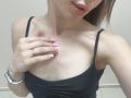 Ramilla's face and chest, showing pink-nailed fingers, a black tank top, and a silver ring, with small moles and pale skin, wearing a silver watch.