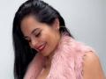 CharlotteCrofort with long black hair, red lipstick, smiling down, wearing a pink furry vest, gold hoop earrings, and a nose ring, looking cute and sexy.