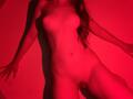 FlyFreedom, naked, standing with red lighting, visible breasts, and a small, exposed pussy, long wavy hair, arms slightly raised, shadow on the wall, soft light on skin.