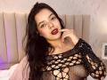 ViolettaRouse with black mesh top showing her tits, red lipstick, finger near mouth, long black hair, light skin, in bedroom, beige headboard, subtle purple wall light.