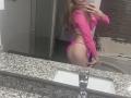 EliseMonet with long blonde hair, pink long-sleeve top, and pink thong, showing her ass in a mirror selfie, holding a phone, in a bathroom with a granite counter.