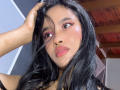 KarolPalacios has black hair, brown eyes, pink eyeliner, pink blush, and pink lipstick. She's touching her hair with one hand, looking up with a slightly pouty expression.