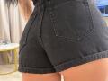 IliriaKara's black denim butt shorts, showing her round ass with visible pockets, cuffed bottoms, and a tattoo on her right arm. Her tan skin is highlighted.