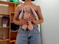 Steisii holding a pink stuffed bunny with long ears, wearing a blue strap top and high-waisted denim skirt, standing in a room with wooden shelves.