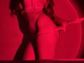 FlyFreedom's ass is highlighted in red lighting, wearing a white thong pulled down to expose her pussy. She's pulling the thong to the side with one hand.
