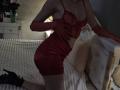 Rozalin in red lace lingerie and matching gloves, kneeling on a bed with white bedding, her hand on her ass, wearing black high heels, her tits slightly visible.