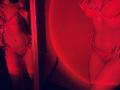 Red-lit photo of Tisia in lace lingerie, showing her tits, pussy, and slim waist. Reflection in mirror shows her from side. Leaves in lace add a touch of nature.