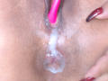 KarlyGreyKiss's wet pussy with a pink dildo partially inserted, white cum dripping down her shaved labia. Her red nails are visible on the right.