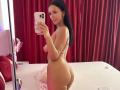 Nadeen's nude selfie showing her curvy ass, small tits, and long dark hair, holding a pink phone, standing sideways in a room with red curtains and white bed.