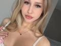 MilagrosEdmisten has blonde hair, blue eyes, pink lips, white strap dress, small tits, hand on chest, gold necklace, and a cute face with long eyelashes.
