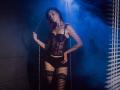 AgataRyili in black lace corset, black panties, and thigh-high stockings, standing on chains, blue smoke around, hands on hips, looking seductive, with her ass slightly raised.