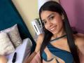 LaurentRay with long black hair, smiling, wearing a blue strappy bikini top, showing small tits, cute nose ring, pink lips, and a sexy smile, sitting on a pink chair.