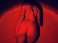 Tisia's back, wearing red lingerie, showing her round ass. Long brown hair, red light, hand on her right cheek, red bra straps visible, soft shadows.