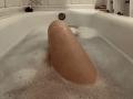 Ein großer, blasser, rosa, schlaffer, unbeschnittener Penis liegt in seifigem Wasser in einer weißen Badewanne..