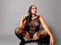 JeimyCampos, squatting, wears black lace lingerie and thigh-high stockings, her brown skin, long braided hair, and red necklace visible. Boobs, pussy, and ass outlined through the lace.