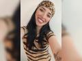 MartinaRey with black hair, wearing a leopard print headscarf and zebra-striped dress, smiling, showing her red lips and tattoo on her right arm, selfie with blurred foreground.