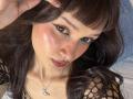 CandyyClair has dark brown wavy hair, a nose ring, and is wearing black fishnet sleeves. Her brown eyes are lined with black eyeliner, and she's looking at the camera.