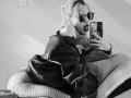 GabySmiith with a butt in checkered pants, wearing a leather jacket and sunglasses, taking a selfie in a mirror, tongue out. Her hair is up in a messy bun.