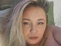 VeraNoires has blonde hair, blue eyes, and a small tattoo on her right shoulder. She's looking at the camera with pouty lips, topless, showing her bare shoulders.