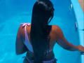 JenifferStar with wet brown hair, back to the camera, wearing a pink and white striped bikini, standing in a blue pool, her ass slightly visible above the water.