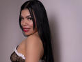 AdrianaPaul with long black hair, pink lipstick, smiling at camera, wearing black mesh lingerie with white lace, looking over shoulder, showing her titties and a small nose ring.