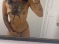 SilvanaXOwen's topless selfie showing tattoos, small tits, brown nipples, black thong, hand covering her pussy, curly dark hair, white door in background, mirror reflection.