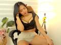 SaschaHelen with long black hair, wearing a black lace bralette and beige shorts, sitting on a chair, eyes closed, hand in hair, small pink vibrator on her lap.