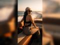 MiilaWx with long black hair, wearing sunglasses, a beige headscarf, black top, and patterned pants, sitting on a boat's tan seat, looking back at the ocean.