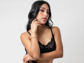 EmmaEstreilla with long black hair, wearing a black lace bra, has her hand near her mouth, looking at the camera, wearing a gold bracelet and necklace.