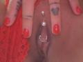 FrenchShanna's pussy with a silver ring and pearl in the labia, fingers with red nail polish, a heart tattoo on one finger, and lace red underwear to the side.