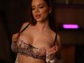 AmalDeyll with large, exposed tits in a sheer, pink lace bra, holding straps, looking down with a slight smile, in a dimly lit room with pink neon.