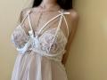 Tisia's big tits in a white lace babydoll with ribbon straps and a tiny bow. She's got a chain necklace over her chest, and her arms are behind her.