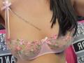FrenchShanna's tits in a sheer pink bra with pink and green floral embroidery, showing a tattoo on her right side and long black hair falling over her shoulder.