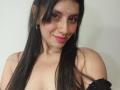 MadissonFontaine with long black hair, pink lipstick, brown eyes, and a forehead jewel, smiling at the camera, showing her bare shoulders and black garment. Boobs visible.