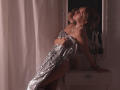 RosaVance with shiny silver sequined dress, pearl necklace, leaning against white dresser, reflecting in mirror, looking up, hand on dress, exposing her ass, in dimly lit room.