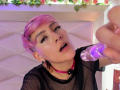 DannyRouds with pink hair, black mesh top, and pink choker, tongue out, holding a purple dildo, small black ear ring, makeup, and short hairstyle, in a selfie.