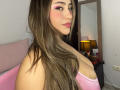 LorensDouce has long brown hair, pink eyeliner, pink lipstick, and a pink top, showing off her tits and a sideboob, standing near a black lamp and mirror.