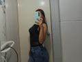 AntoniaBrunni with red hair, black sleeveless top, sheer midsection, and blue jeans, taking a mirror selfie, covering her face with a blue phone, showing her ass.
