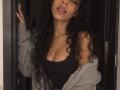 GabyAndVictor has curly black hair, a tan skin tone, and is sticking out her tongue. She's wearing a black tank top, gray hoodie off-shoulder, showing her boobs.