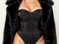 Angelina Deleon trägt einen schwarzen, trägerlosen, transparenten Body, der ihre Brüste zeigt, eine schwarze Pelzjacke und eine Perlenkette, vor einem schlichten Hintergrund..