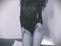 Black sheer long-sleeve top, black high-cut panties, curly dark hair, hands on thighs, ring on left hand, bare legs, monochrome, soft light, SweetClaraa.