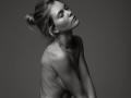 EolantaMarina with her eyes closed, head tilted back, and blonde hair in a messy bun, topless, showing her small tits and slim, pale body in a black-and-white shot.