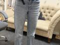 Dalaila's blue jeans, showing a slight bulge in the crotch area, standing in front of a beige tufted sofa, with a gray office chair to the left.