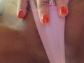 FrenchShanna's pink panties, pulled to the side, showing her pussy. Her hand with red nail polish rests on her bare, tanned, hairy-ass. Her fingers have a small tattoo.