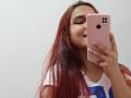 AntoniaBrunni with red hair, pouting lips, holding pink iPhone, white shirt, looking in mirror, taking selfie, showing ass, hand on phone, light skin, casual, soft lighting.